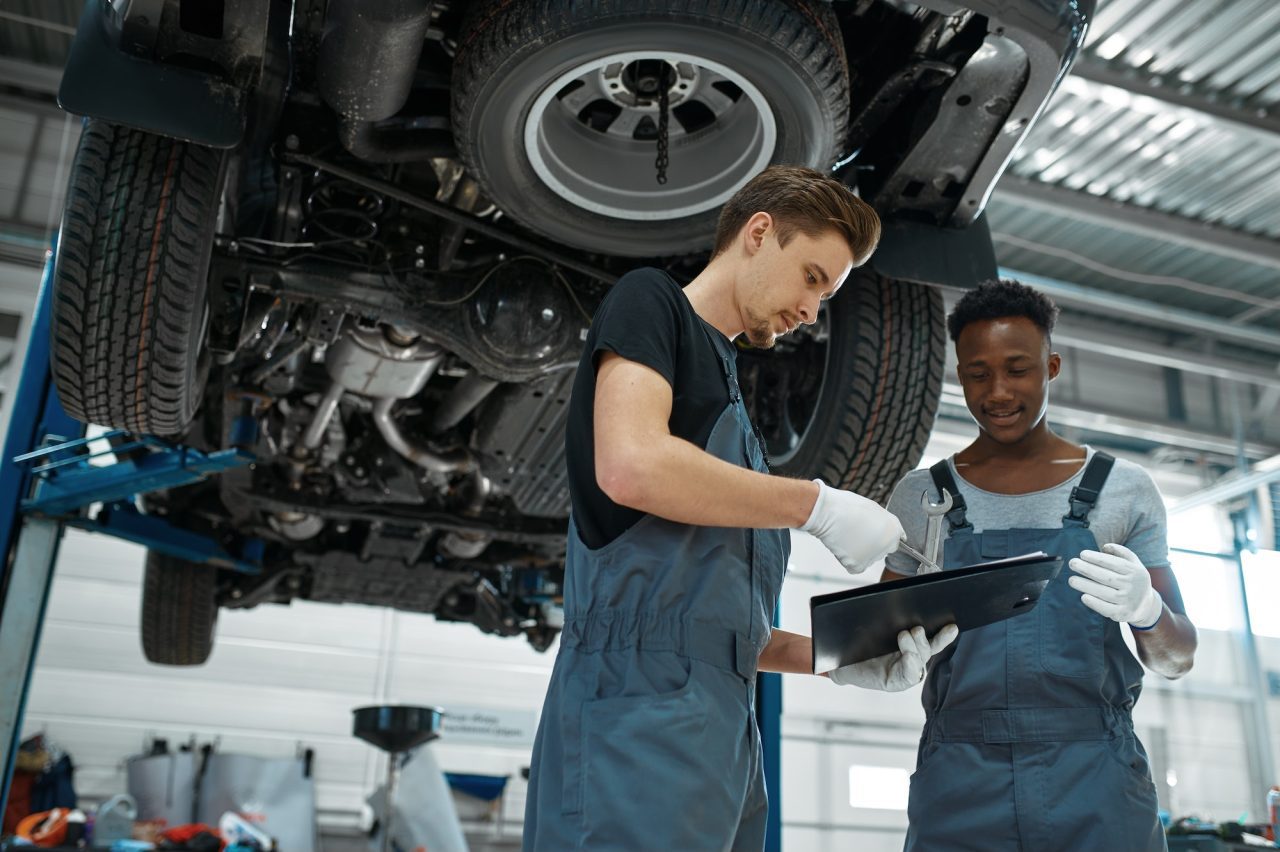 mechanics reviewing paperwork standing underneath raised car