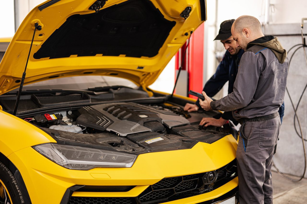 two mechanics inspecting a car under the hood